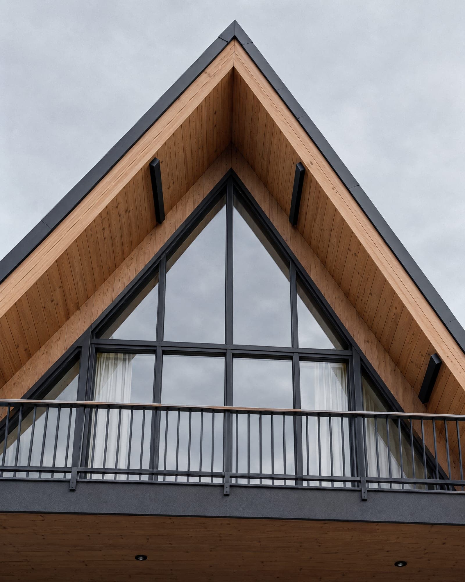 Looking up at the gable balcony of an AFRME: black steel rail, larch soffit converging toward the ridge