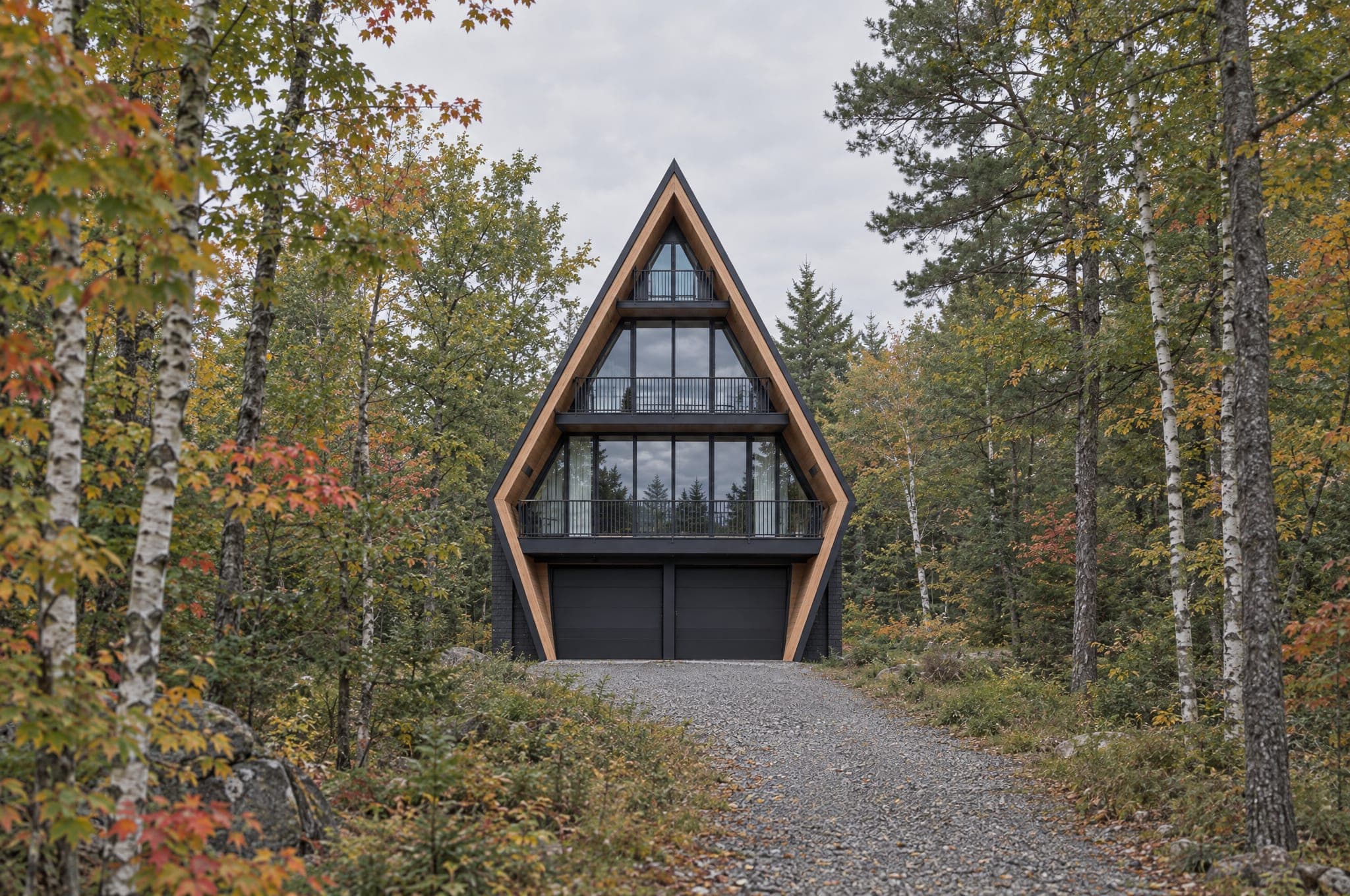 The Four seen from David Thompson Drive: a four-story kicked A-frame with two garage doors at the base, larch gable and balconies, among birches and maples