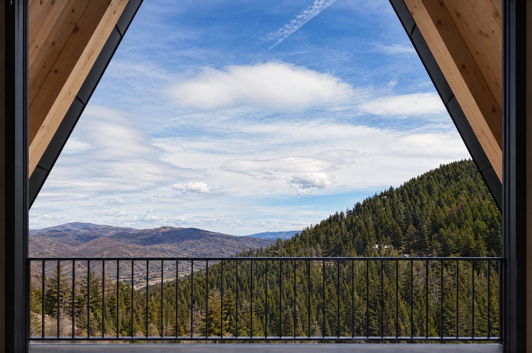 The view from a balcony of The Four in Summit Park: larch reveal and black rail in the foreground, forested ridges and the valley under a wide sky